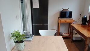 Une petite cuisine avec une table en bois, une chaise blanche, une plante en pot, un réfrigérateur noir et un four à micro-ondes posé sur la table en bois.