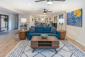 A modern living room with a blue sofa, wooden coffee table, and a large abstract painting.