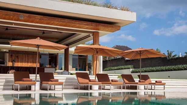 A modern outdoor pool area with lounge chairs and umbrellas, a wooden deck, and a view of the surrounding landscape. - Where Tranquility Meets Luxury – Bali Villa 1071 (Bali)