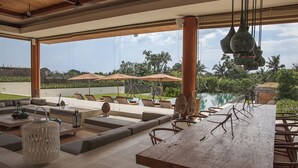 A spacious outdoor seating area with a pool view, wooden furniture, and hanging pendant lights. - Where Tranquility Meets Luxury – Bali Villa 1071 (Bali)