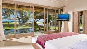 A hotel room with a large window offering a view of a tropical landscape, a bed, and a television on the wall. - 5-Star Beachfront Villa, Bali Villa 1014 (Bali)