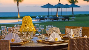 A table set for a meal with a decorative yellow flower centerpiece, surrounded by wicker chairs and a view of the ocean. - 5-Star Beachfront Villa, Bali Villa 1014 (Bali)