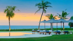 A beachside resort with lounge chairs and umbrellas, palm trees, and a view of the ocean. - 5-Star Beachfront Villa, Bali Villa 1014 (Bali)