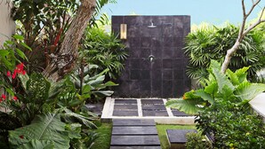 A modern outdoor entrance with a dark door, surrounded by lush greenery and a stone pathway leading to a small seating area. - Elegant Cliffside Villa with Breathtaking Views – Bali Villa 1031 (Bali)
