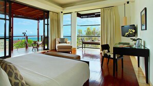 A spacious bedroom with a large bed, a desk, and a chair. There is a balcony with a view of the ocean. - Elegant Cliffside Villa with Breathtaking Views – Bali Villa 1031 (Bali)
