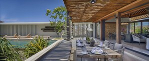 An outdoor dining area with a pool, wooden pergola, and modern furniture. - Bali Villa 1082: Cliffside Luxury with Ocean Views (Bali)