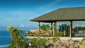 Een modern huis met een groot raam, een houten terras en uitzicht op de oceaan.