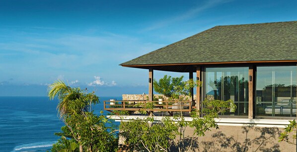 A modern house with a large glass window, a wooden deck, and a view of the ocean. - Bali Villa 1082: Cliffside Luxury with Ocean Views (Bali)