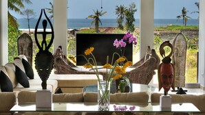 Una sala de estar con vista al océano, que incluye un sofá, una mesa de centro y elementos decorativos como un jarrón con flores y una escultura.