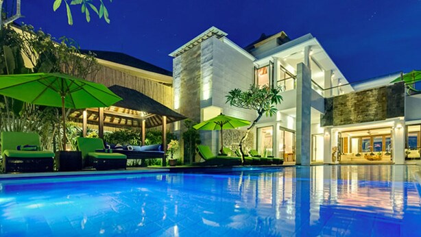 Un hotel moderno con piscina, sillones de exterior y sombrillas.
