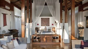 A spacious room with a wooden ceiling, a bed with a canopy, a dining area with a table and chairs, and a seating area with a sofa and armchairs.
