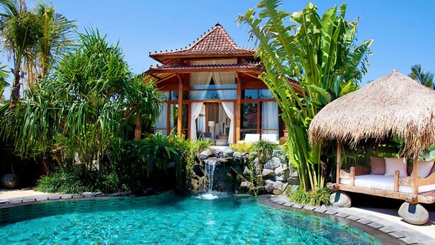 A resort with a swimming pool, a thatched-roof hut, and lush tropical vegetation.