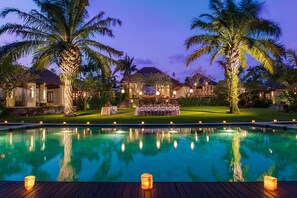 A poolside view at dusk with a dining area and palm trees.