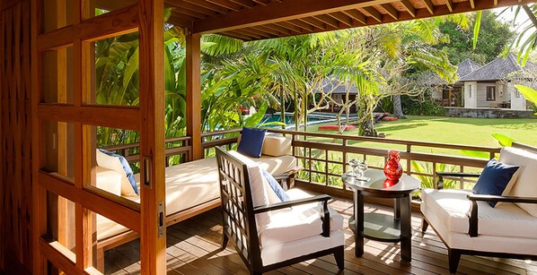 A wooden deck with two white sofas and a small table, overlooking a pool and lush greenery.
