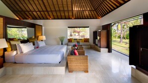 Un'ampia camera da letto con un letto grande, un angolo relax con divano e vista su un giardino attraverso una grande finestra.
