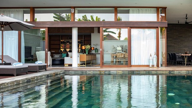 A modern house with a swimming pool, a dining area, and a living room with a sofa and a TV. - Stylish Beachside Villa with Pool & Stunning Views – Bali Villa 1068 (Bali)