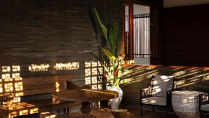 A room with a high ceiling, wooden beams, and hanging woven light fixtures. There is a large potted plant in the center, a wooden bench, and a round table with chairs. - Stylish Beachside Villa with Pool & Stunning Views – Bali Villa 1068 (Bali)