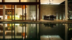 A modern indoor pool area with a dining setup and a view of the night sky. - Stylish Beachside Villa with Pool & Stunning Views – Bali Villa 1068 (Bali)