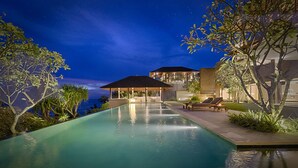 Vue nocturne d’un espace piscine luxueux, avec un coin salon abrité et des chaises longues.