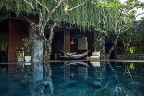 Un'area piscina interna tranquilla con un'amaca, pareti in pietra e rigogliosa vegetazione.