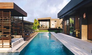 A modern pool area with a clear view of the pool, lounge chairs, and a building with large windows.