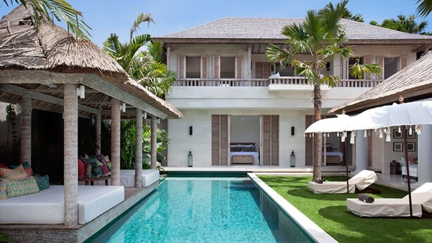 A poolside area with a clear pool, lounge chairs, and a thatched roof structure. - Serenity by the Shoreline – Bali Villa 1048 (Bali)