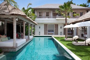 A poolside area with a clear pool, lounge chairs, and a thatched roof structure.