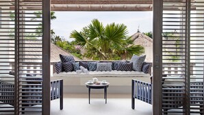 A covered outdoor seating area with a view of tropical vegetation and thatched-roof buildings. - Serenity by the Shoreline – Bali Villa 1048 (Bali)