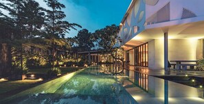 Ein modernes Haus mit Swimmingpool, umgeben von üppiger Vegetation und einem gut beleuchteten Außenbereich.