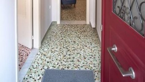 Un pasillo con una puerta roja, piso estampado y una silla azul al fondo.