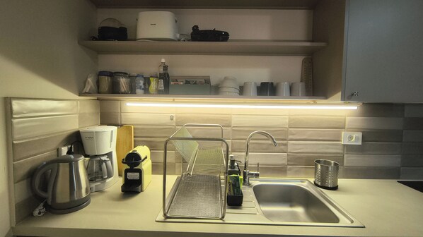 A kitchen with a sink, a coffee maker, a kettle, and a range hood.