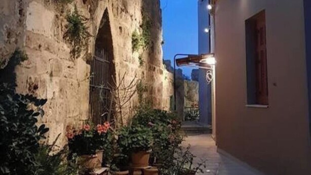 Un estrecho callejón con un muro de piedra a un lado y un edificio al otro. Hay plantas en macetas y una verja de metal.