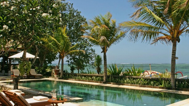A poolside area with lounge chairs, a clear view of the ocean, and a tropical garden setting.