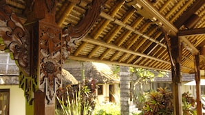 A wooden structure with intricate carvings and a thatched roof, surrounded by lush greenery.