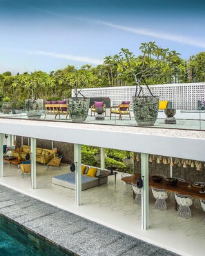 Een modern buitenverblijf met een zwembad, met een witte balustrade, meerdere stoelen en grote plantenbakken.