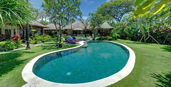 Una piscina de borde curvo, rodeada de césped cuidado y plantas tropicales.