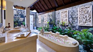 A luxurious bathroom with a freestanding bathtub, a large mirror, and a stone wall with intricate carvings.