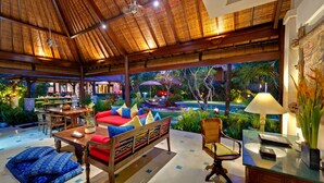 A spacious indoor area with a thatched roof, a pool, and outdoor seating.