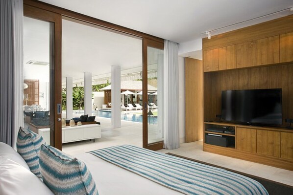 A modern hotel room with a large bed, a TV, and a view of an outdoor pool area.