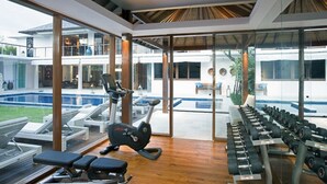 Et moderne fitnesscenter med træningsudstyr, en pool og udsigt til en boligbygning.