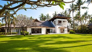 Una casa de dos pisos con un jardín grande, rodeada de palmeras.