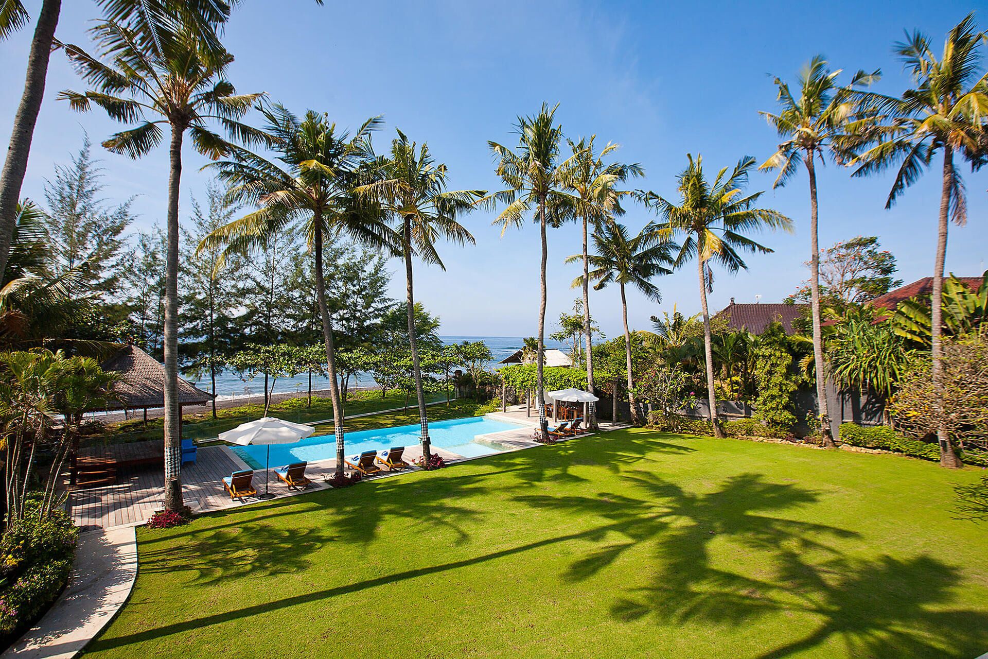 A pool area with lounge chairs, palm trees, and a view of the ocean.