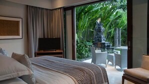 Ein Schlafzimmer mit Bett, Fernseher und Blick auf einen Garten mit einem Wasserspiel.