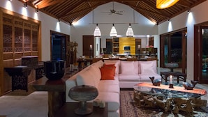 A spacious living area with a high ceiling, a central seating area with a white sofa, a glass coffee table, and a wooden dining table.