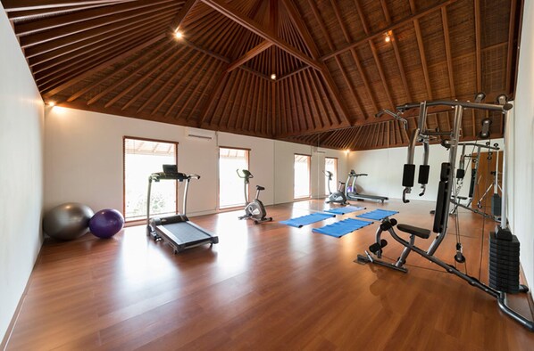 A spacious gym with wooden flooring, exercise equipment, and large windows.