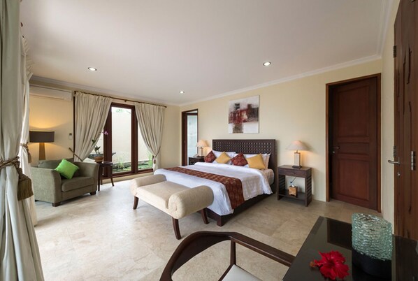 A hotel room with a large bed, a sitting area with a chair and a table, a bedside table with a lamp, and a view through the window.