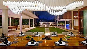 A restaurant with a long dining table set for a meal, surrounded by a well-lit outdoor area with a pool and lounge seating. - Exclusive Luxury Villa with Pool & Entertainment – Bali Villa 1059 (Bali)