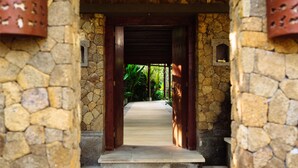 A stone pathway leading to a wooden door with a metal gate, surrounded by stone walls and greenery.