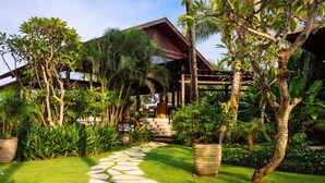 A tropical resort with a stone pathway leading to a wooden structure surrounded by lush greenery and palm trees.