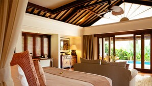 A spacious bedroom with a large bed, a smaller bed, a nightstand, a lamp, and a view of a pool.